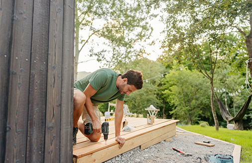 Guy outside drilling and building new deck for home.